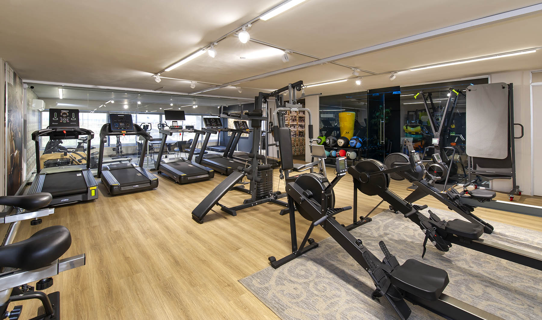 A wide view of the Express Fitness Urban showroom with a light wood floor. The space features a lineup of treadmills on the left, with two rowing machines and a multi-station functional trainer in the centre.